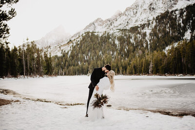 winter wedding withthe bride and groom on the snow while kissing in front  of  a mountain range in Jackson Hole
