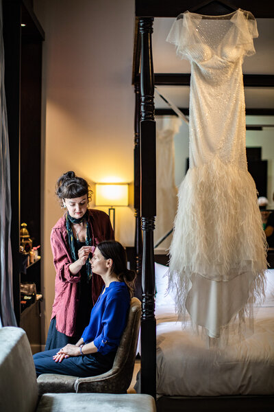bride having her make up done with dress hanging up