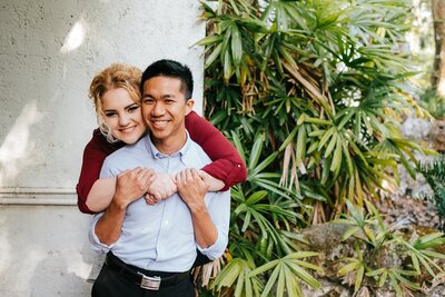 Shannon Lee, an Orlando wedding photographer capturing a playful and loving moment of an engaged couple, with the bride piggybacking on her partner in a tropical setting.