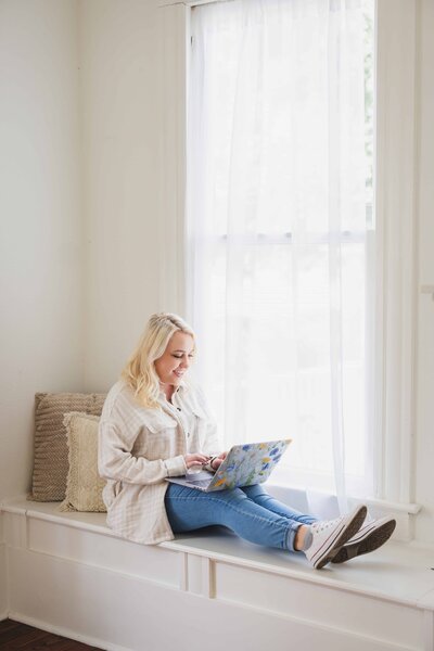 Girl sits in bright window with laptop