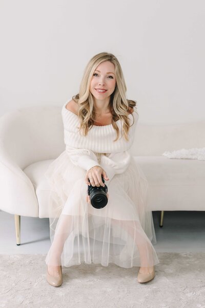 Kristie Lloyd sits on a white couch in her photography studio