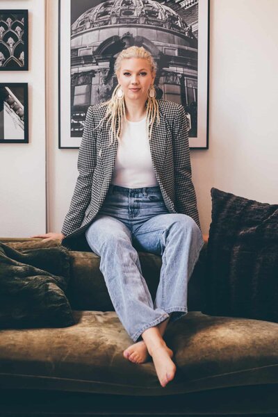 A woman sitting on a couch in jeans and a blazer, captured by a skilled Shreveport branding photographer Britt Elizabeth.