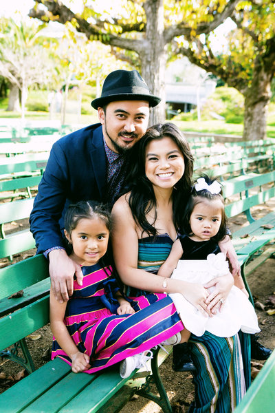 Family of four sit on a green bench smiling at the camera
