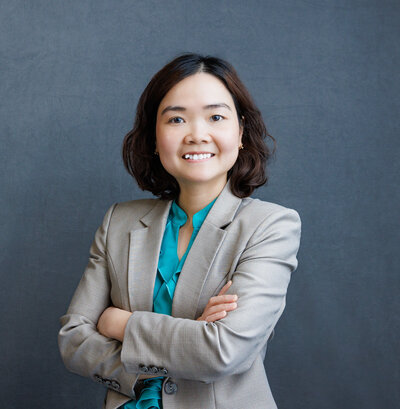 a woman smiling in a colorful shirt and gray blazer