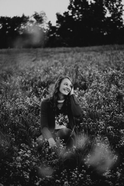 A girl sitting in a field of flowers and smiling over her shoulder