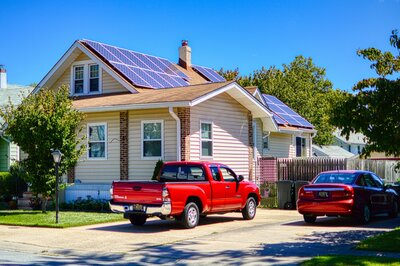 Single-family home with rooftop solar panels and parked vehicles in a residential neighborhood under clear blue skies