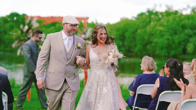 Bride and groom walking down the aisle outdoors with trees behind them