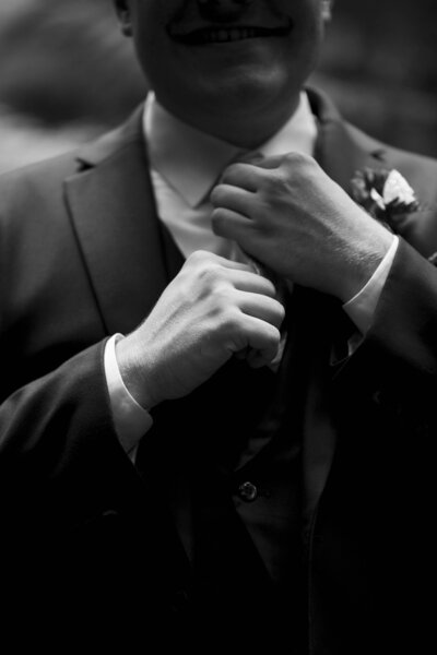 Groom is tightening his tie while prepping for his wedding
