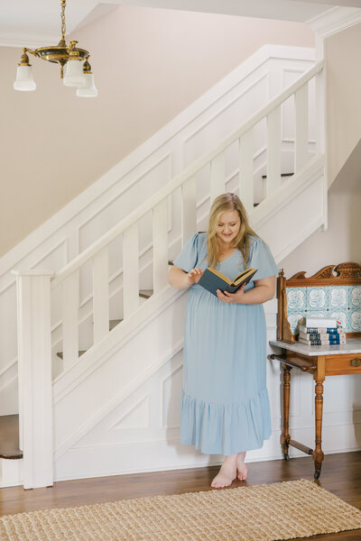 Woman in a light blue dress reading a Bible in front of a white staircase