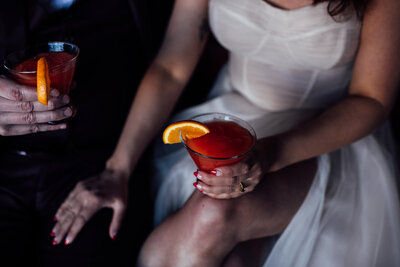 Two people standing close holding cocktails.