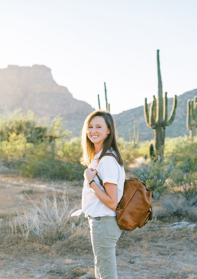 woman standing in the desert holding a leather backpack
