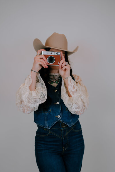 woman wearing a cowgirl hat while holding a camera up to her eyes