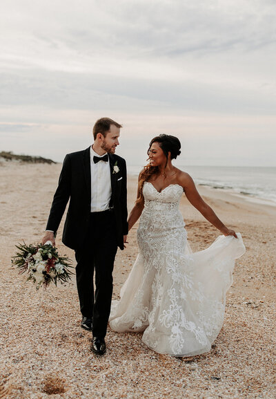 Bride and groom walking along the shoreline after a coastal ceremony, a romantic wedding moment planned by The Eventful Gals.