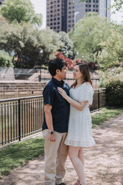 A happy couple embraces during their engagement session on Brown's Island in Richmond, Virginia, with lush greenery and city views in the background, captured by Quinn Photography LLC.