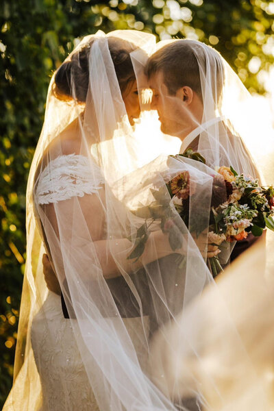 bride and groom posed during golden hour under her custom pearl bridal veil blusher