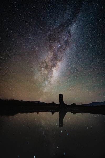 A couple reflected in a pond with the milky way behind them