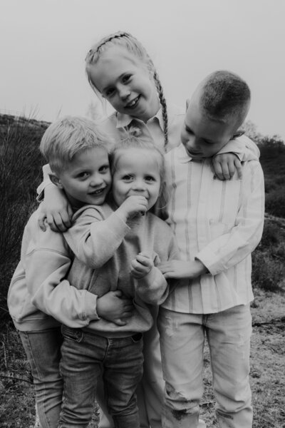 Drie kinderen omhelzen elkaar in een veld, omringd door groen gras en een heldere lucht.