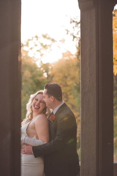 Portrait of a couple sharing a laugh as they are sunkissed during golden hour and the bride's red lipstick shines through the sunlight