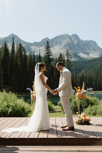 Bride and groom hold hands at alter during their fernie wedding at island lake lodge