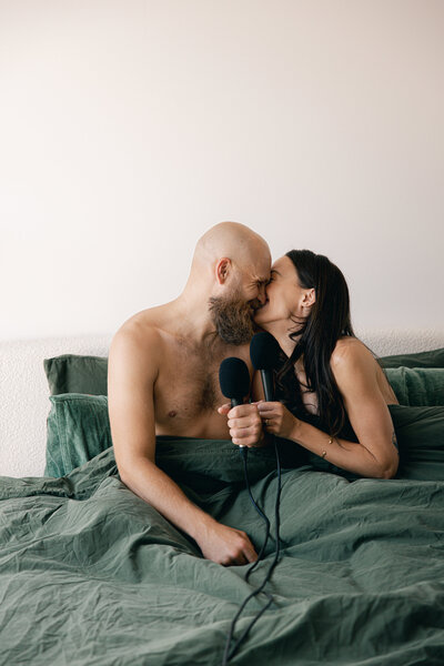 Relationship and intimacy coach with husband sitting in bed kissing with a podcast microphone