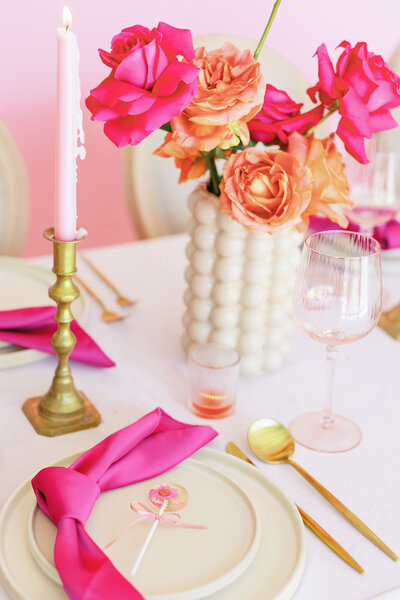 Table setting with gold silverware, pink napkins, pink candles, and pink and orange floral centerpieces