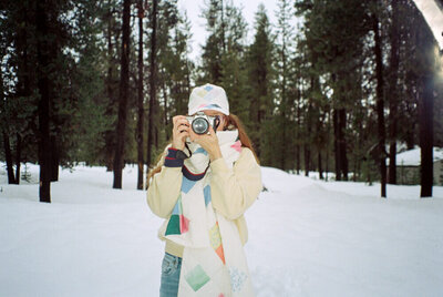 Eugene wedding photographer, Heather, holds a camera up to take a picture while out in the snow. 