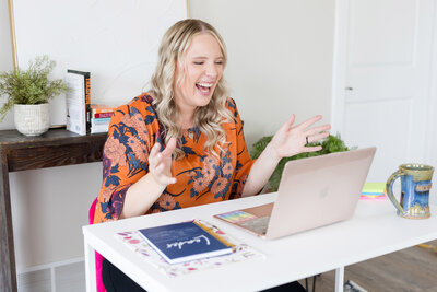 Becca excitedly smiling as she talks to someone on her laptop