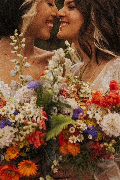 A couple, both holding vibrant bouquets, stand close together, smiling at each other tenderly in Flagstaff Arizona.