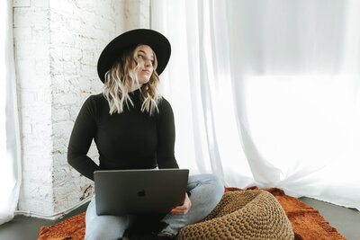 Blonde girl with black hat sitting with computer in her lap