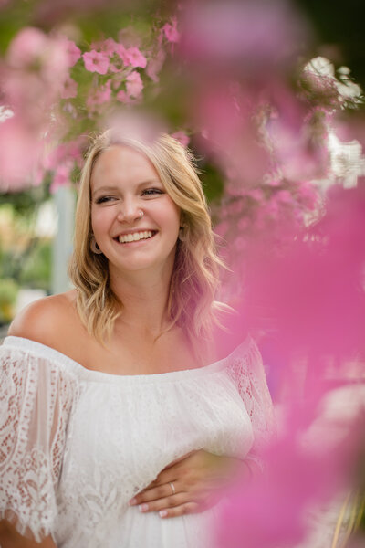 Maternity session of blonde mother laughing with flower bokeh in front