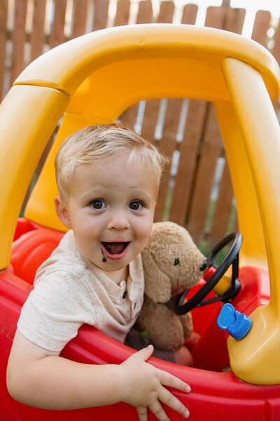 Blonde little boy looking at camera sitting inside play car