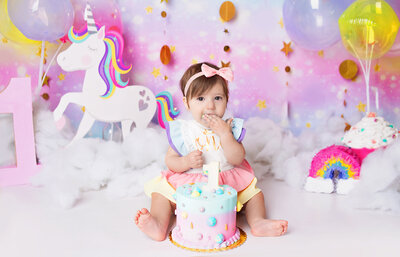 Little girl wearing pastel romper eating cake during cake smash photoshoot in Mount Juliet Tennessee photography studio