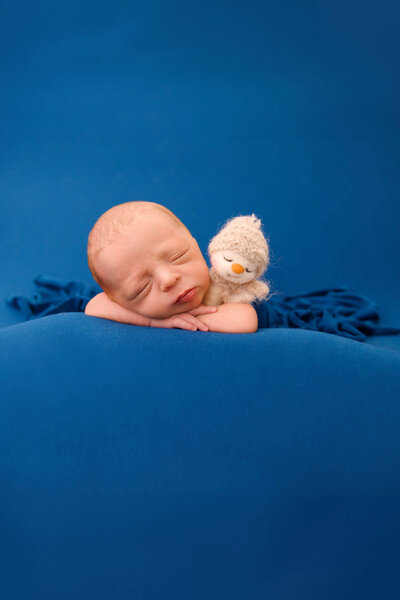 newborn baby boy holding a snowman lovie on a blue background for his newborn photos.