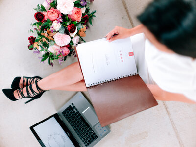 Event planner Linda seated with a spiral-bound proposal and laptop beside a colorful floral bouquet.