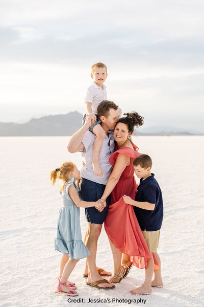Kate Simpson’s family stands together on a vast white salt flat, the parents embracing their three children with a joyful expression as they enjoy a moment together.