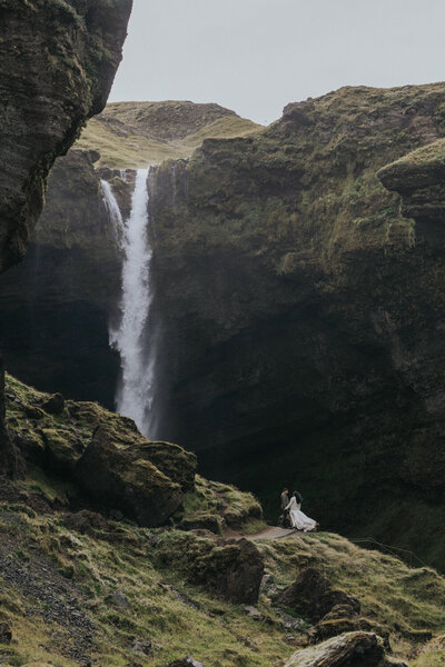 Couple climbs a mountain near an Icelandic waterfall