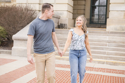 A young couple holding hands at the state capitol, looking at each other and smiling.  Male is wearing a blue shirt and khaki pants with brown hair.  Female is blond with blue jeans and a white and blue shirt.