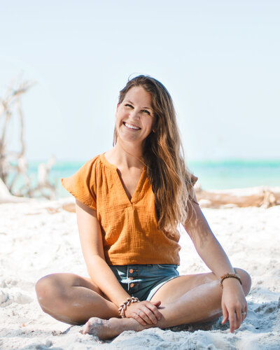 Cassie Wegeng Photography sits on beach facing camera
