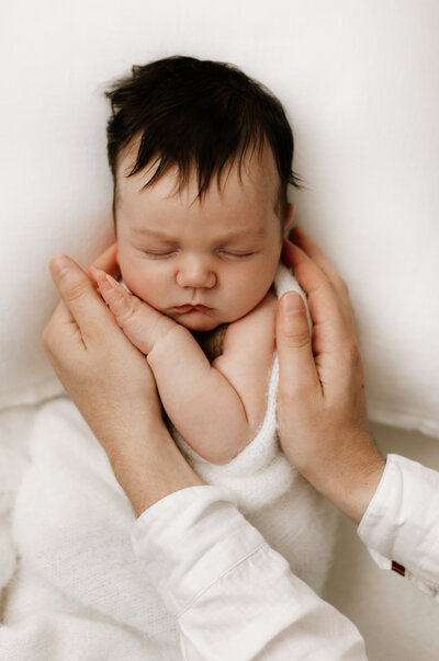 Close-up newborn photo featuring a baby cradled gently in parent's hands, captured in soft natural tones by a Sydney newborn photographer.