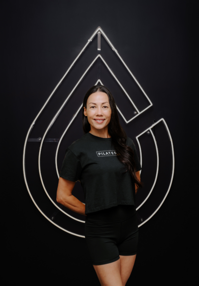 Headshot of Pilates instructors Amber standing in front of Pilates214 neon logo sign.
