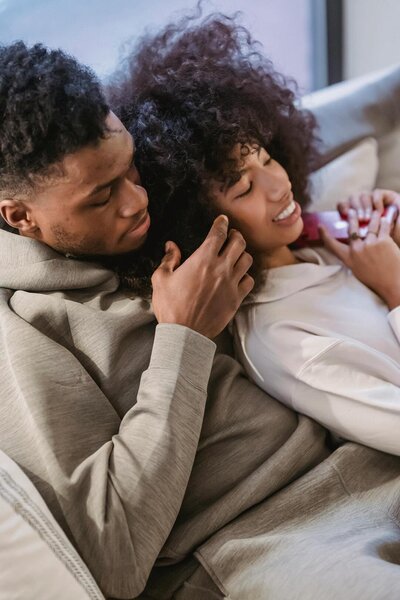 Black couple smiling while laying on the couch
