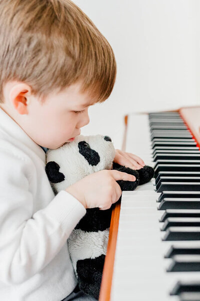 Boy plays piano with his stuffed panda bear