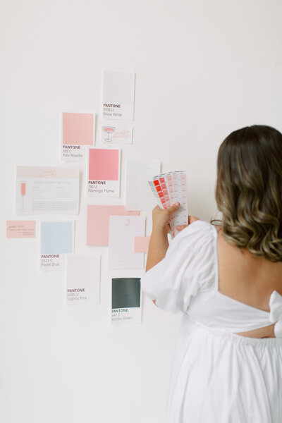 Brunette woman wearing white dress placing PANTONE swatches on the wall