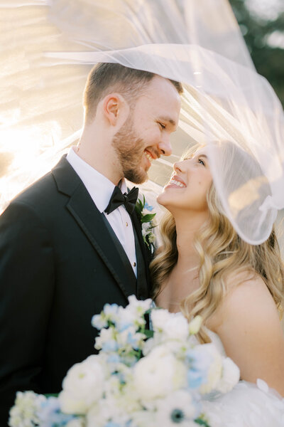 Bride and groom with their faces close smiling at each other underneath the bride's veil