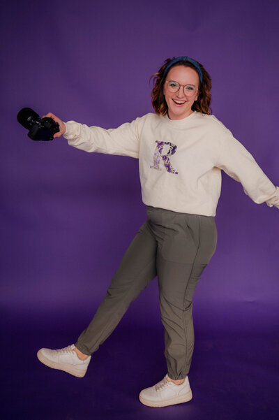 Rachel Hahn, owner, poses against grey brick wall smiling at the camera with her hands in her hair.