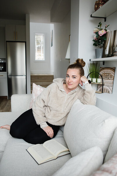 Realtor Tamara Rzan relaxing on a gray sofa, surrounded with an inviting ambiance of a cozy white home
