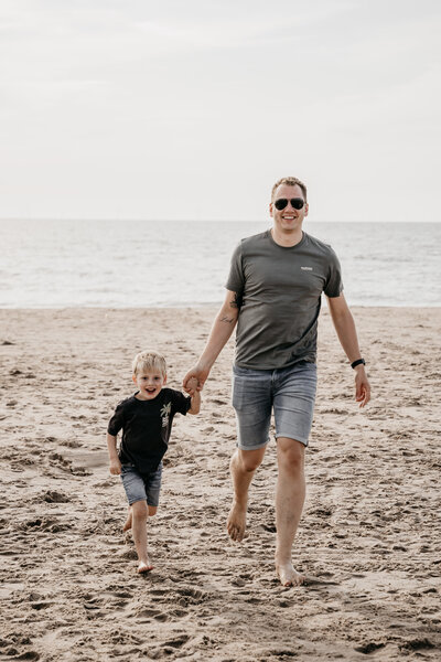 Vader rent met zoontje over het strand tijdens zonsondergang.