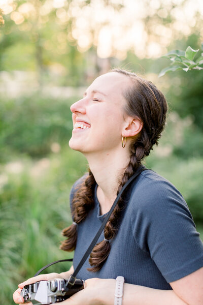 Girl with two braids laughing and holding a film camera in Madison, Wisconsin