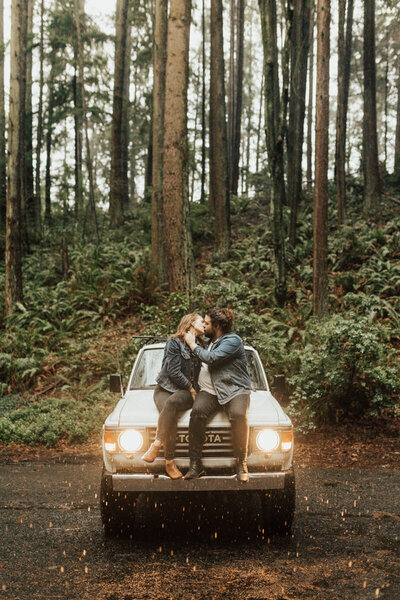 couple kissing on their car in the woods
