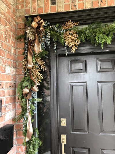 Custom Holiday outdoor decorating around a black door with cedar sprays and gold accents by Helena's Gardening